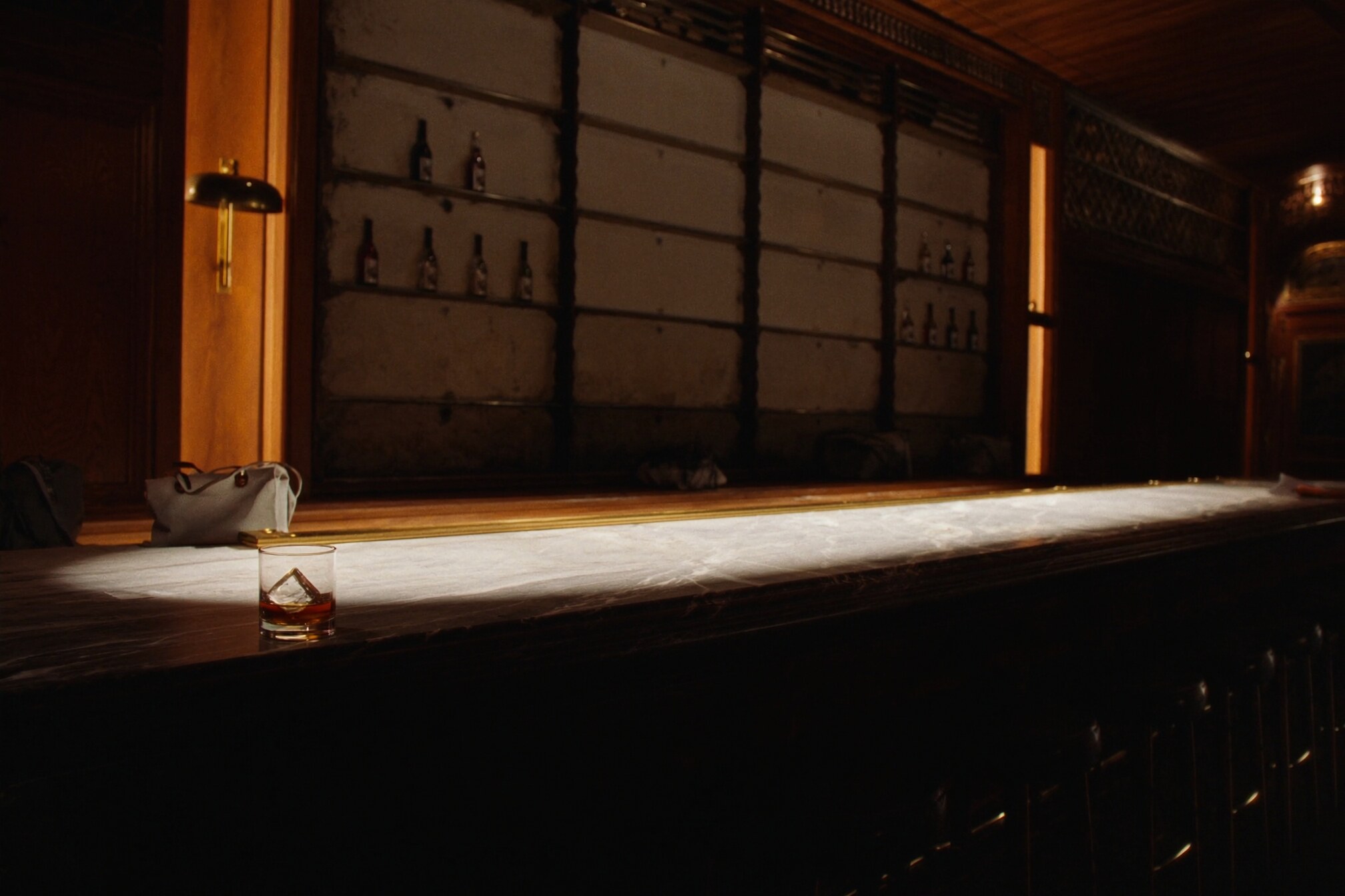 A long marble bar under a single spotlight, one glass waiting on the counter