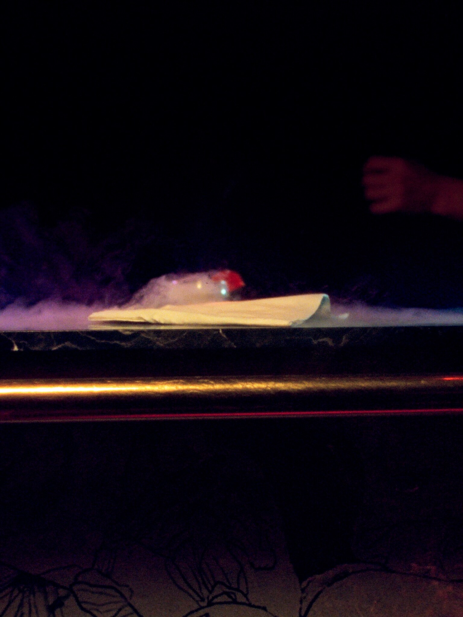 The bar at night: brass rail, marble edge and a cocktail under smoke