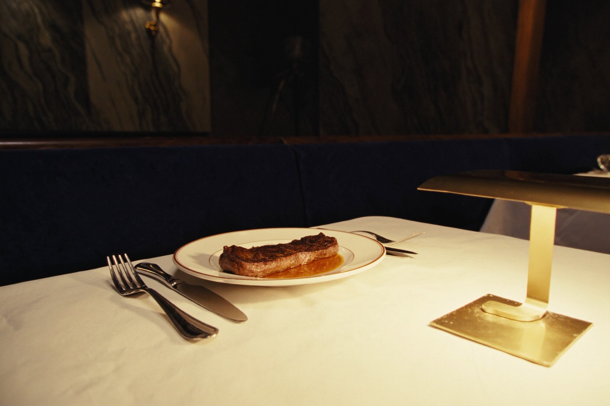 A table set in cream linen with a plated steak and a low brass lamp