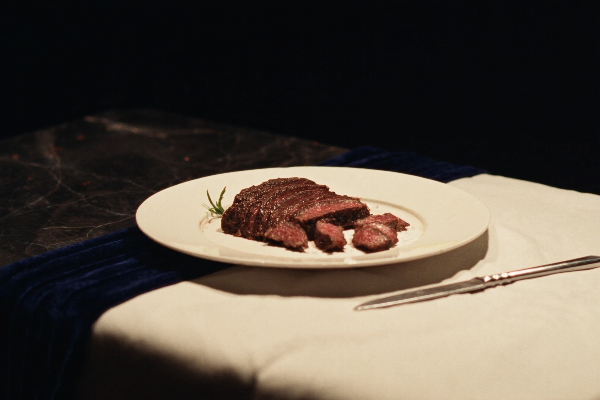 Sliced steak on a cream plate over linen and a navy velvet runner