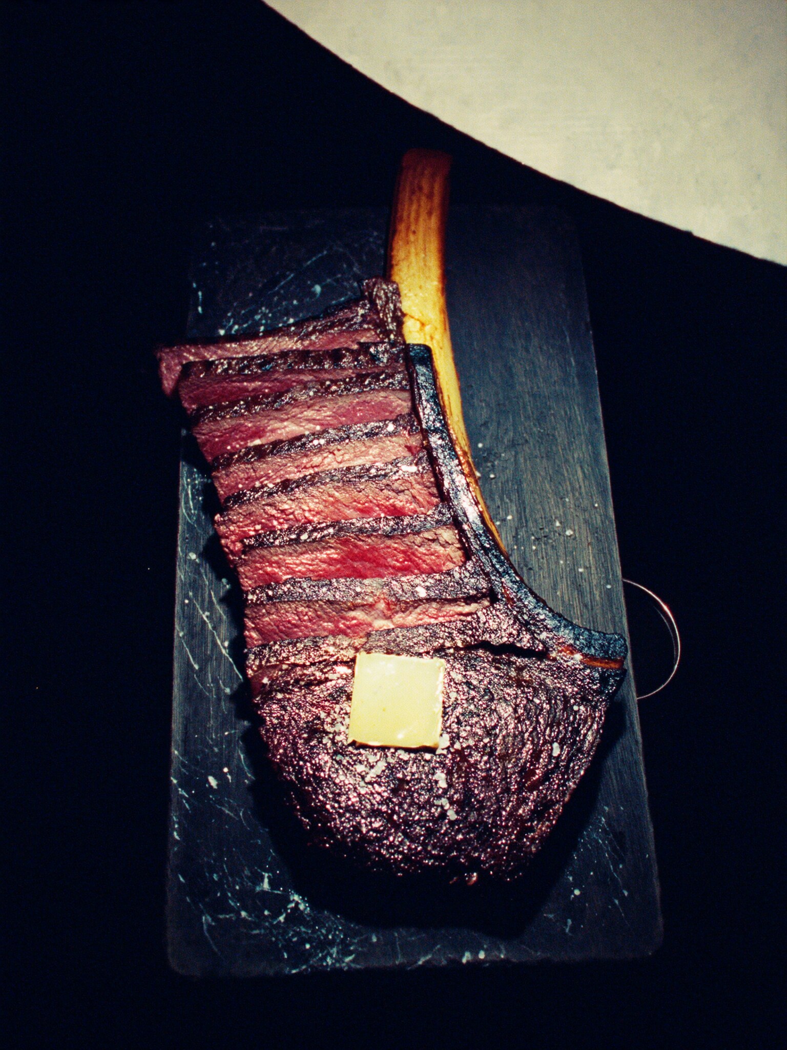 A sliced tomahawk steak on a dark wood board seen from directly overhead